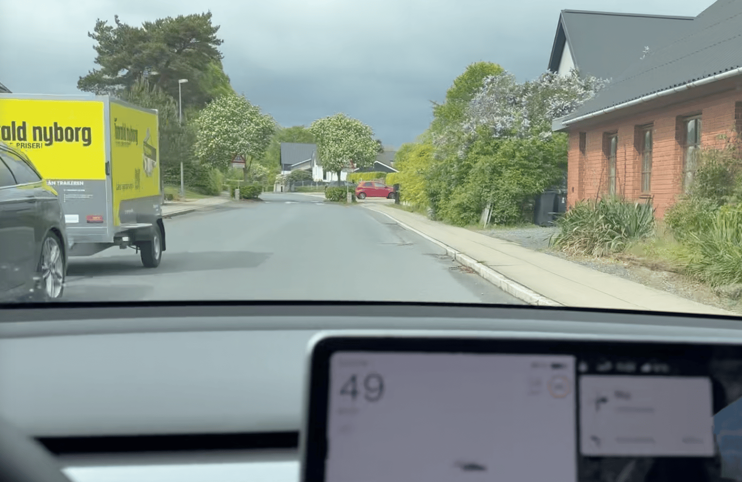 Still fra video taget ved 49 km/t. Det trekantede advarselsskilt om krydsende cyklister er skjult bag løvet i trækronerne i helleanlægget