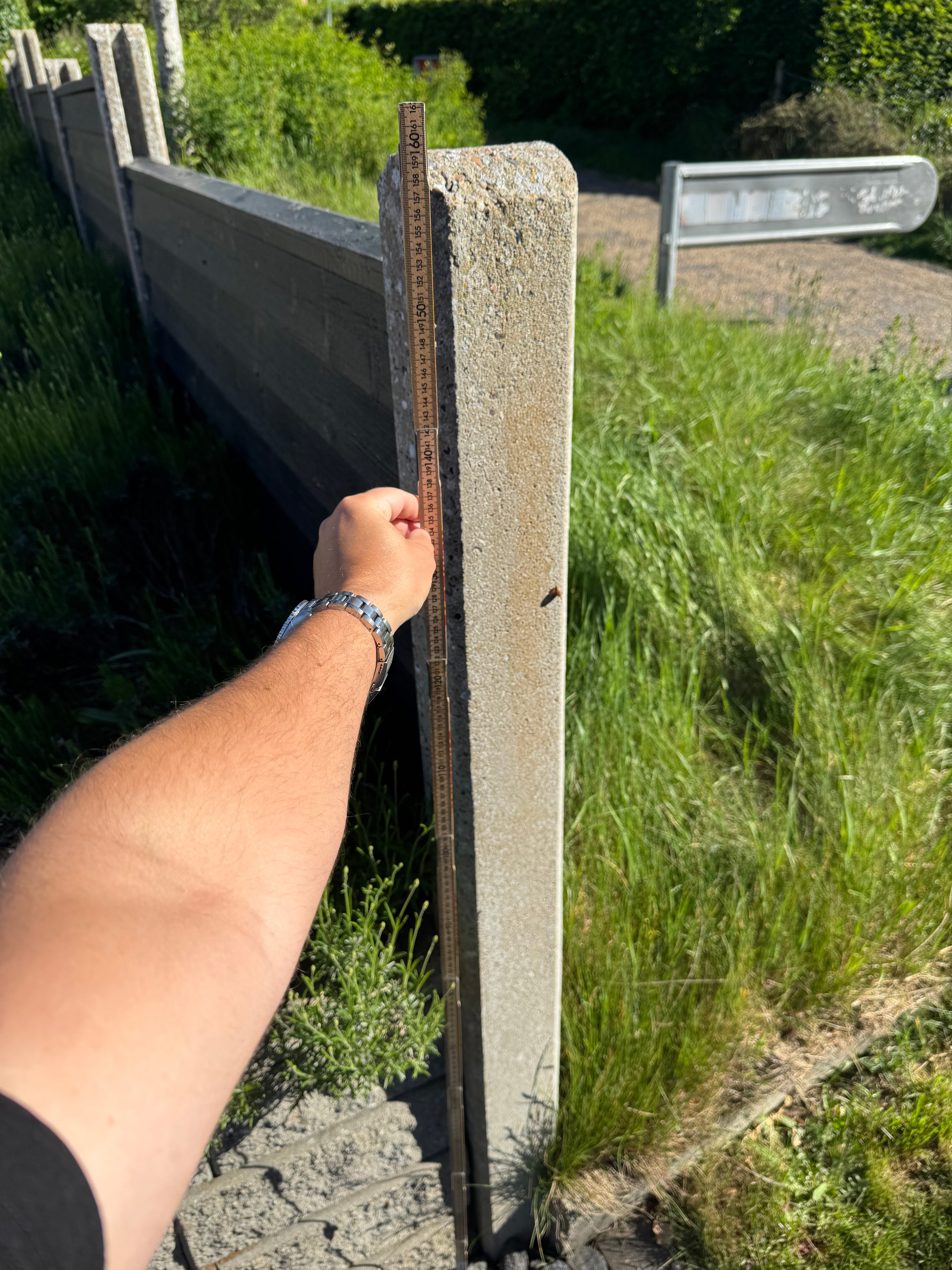 Tommestok holdt op mod et stakit på hjørnegrunden. Stakittet måler 150 cm, søjlerne 159 cm