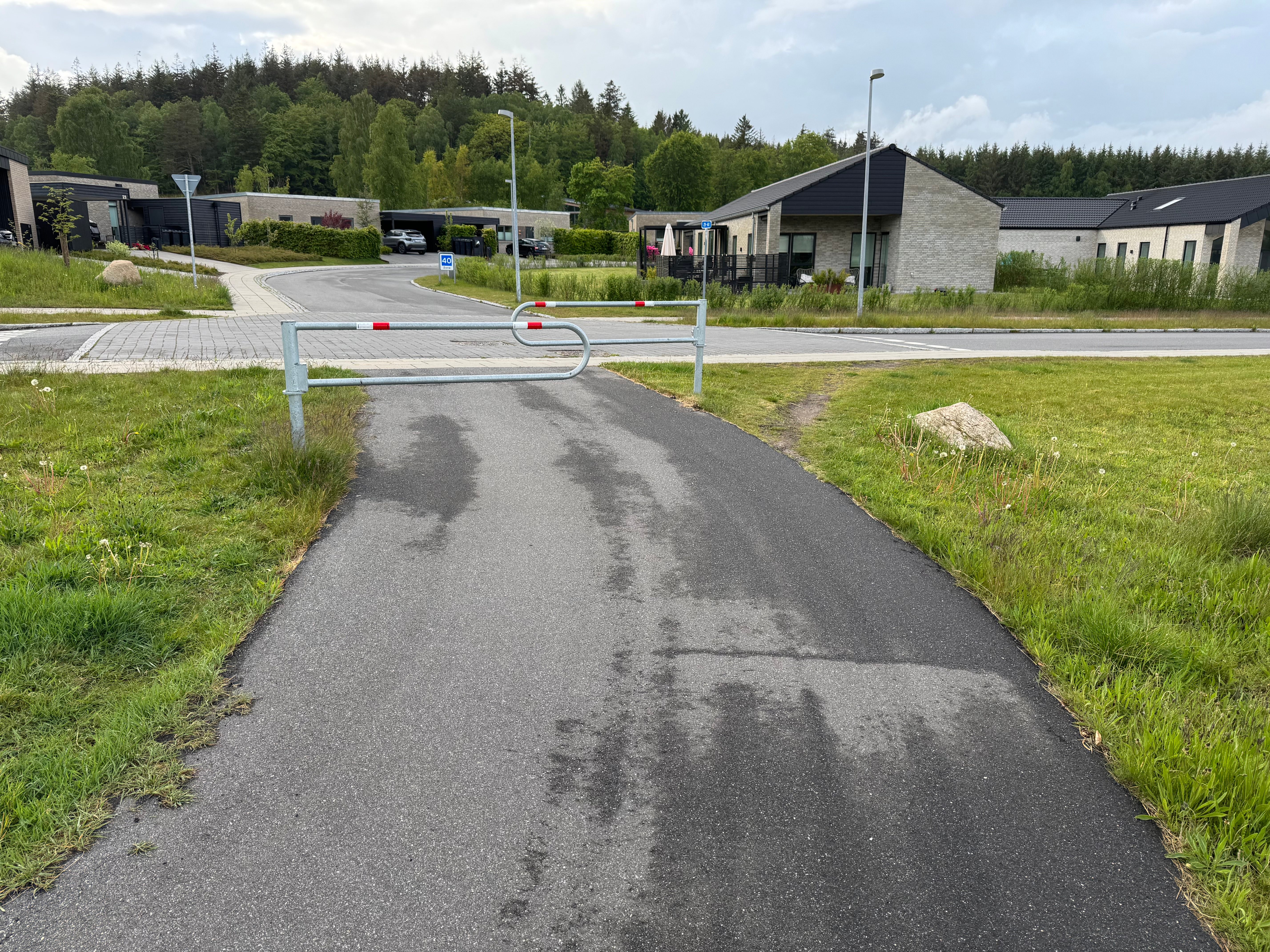 Hjortespringet-bom set i lige perspektiv mod kvarteret. Bare jordzoner langs stiens kanter viser hvor cykelhjul har kørt udenom bommen